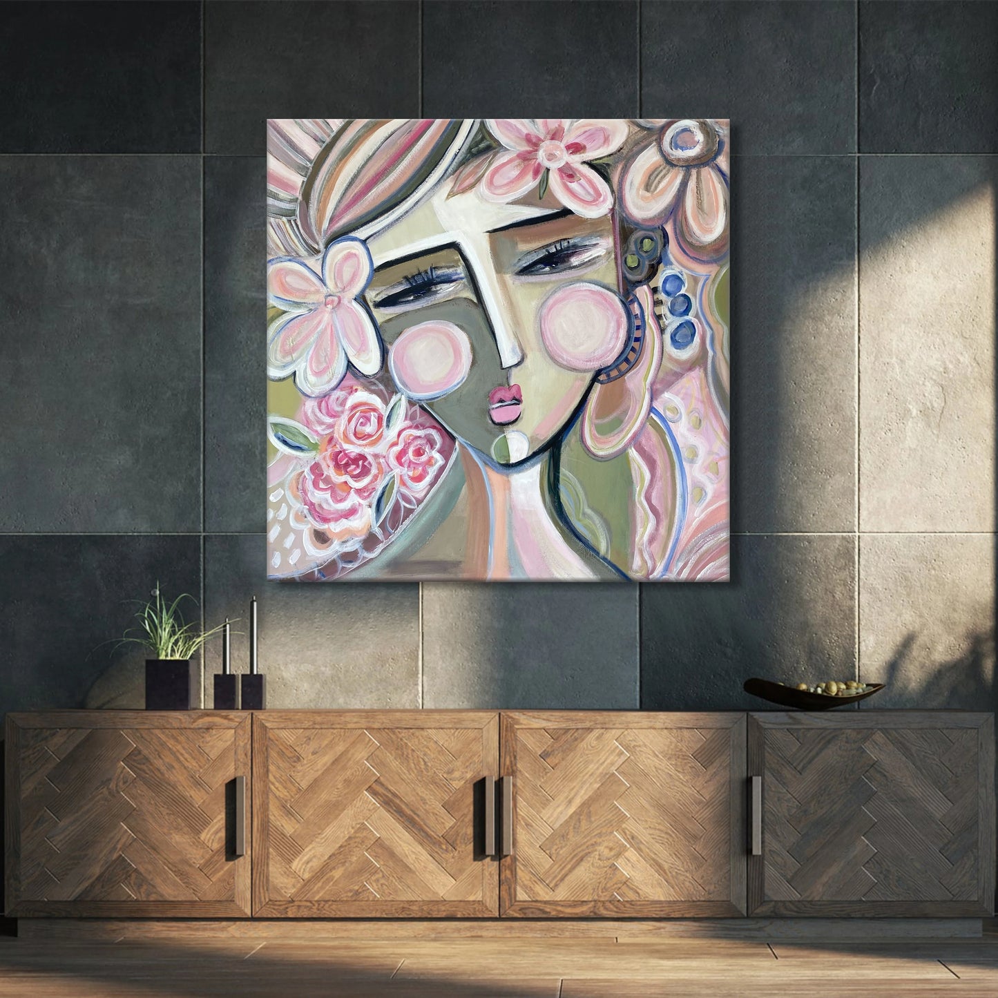 a large abstract painting of a woman's face with floral elements, hanging on a wall above a wooden cabinet.