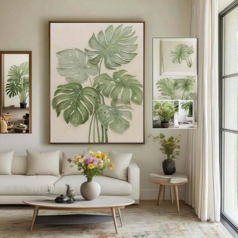 a living room with a large framed painting of green leaves on the wall, a white sofa, a coffee table with a vase of flowers, and a window with white curtains.