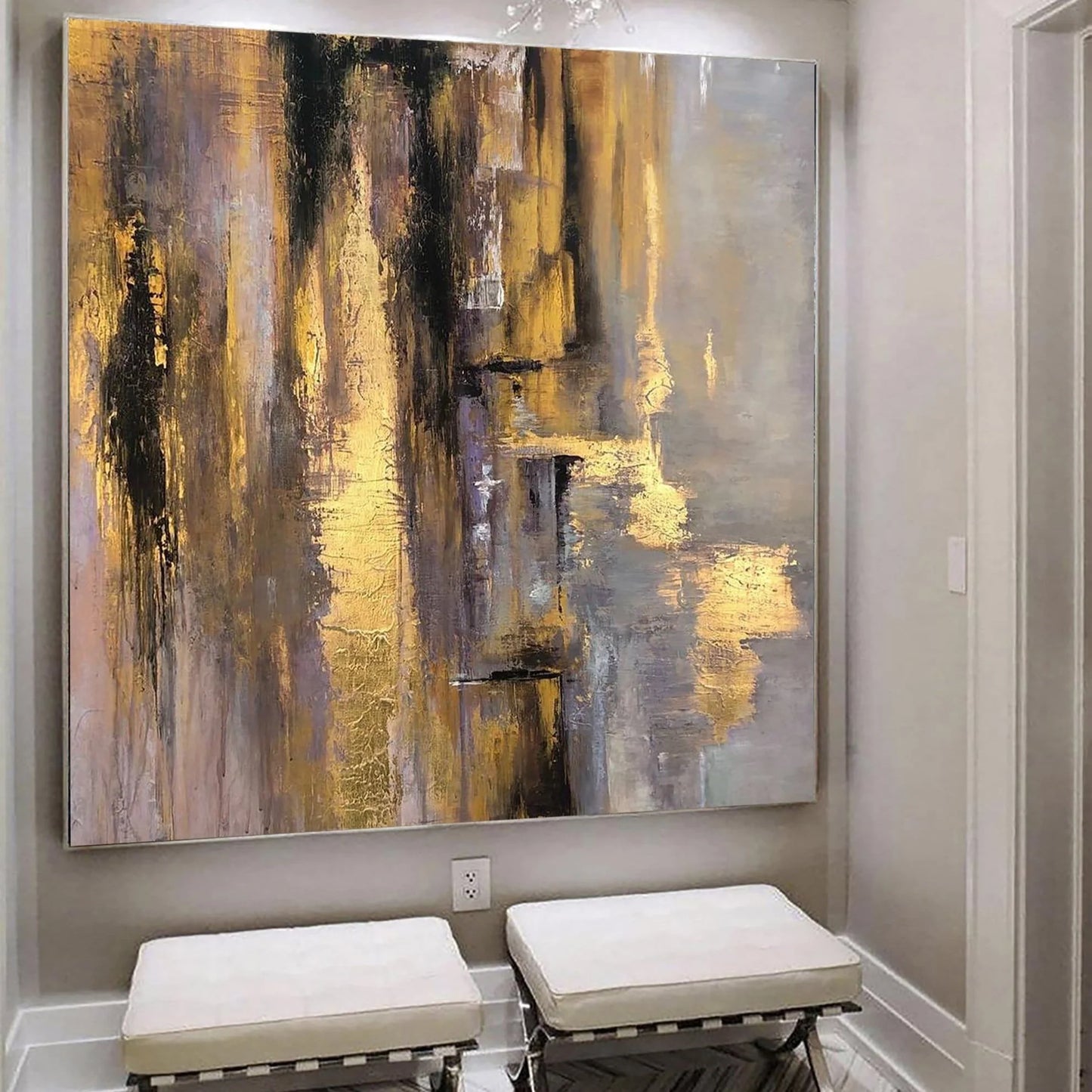 a large abstract painting with a mix of warm and cool colors, including shades of yellow, orange, and gray, creating a vibrant and dynamic visual effect. The painting is displayed on a wall, and there are two white ottomans placed in front of it, providing a comfortable seating area for viewing the artwork.