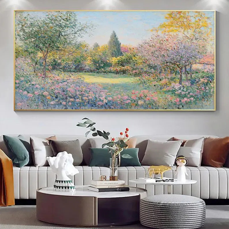 a large painting of a colorful garden scene hanging on a wall above a white sofa with decorative pillows. The painting depicts a lush, vibrant landscape with trees, flowers, and a pond. The sofa is positioned in front of the painting, creating a cozy and inviting atmosphere in the living room.