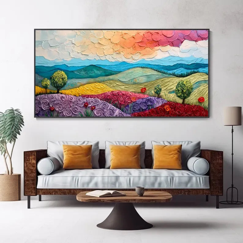 a large, colorful painting of a landscape with mountains, flowers, and trees hanging on a wall above a couch in a living room setting.