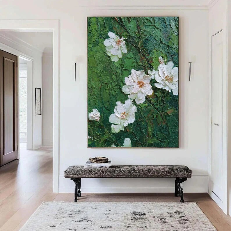a large painting of white flowers on a green background hanging on a wall in a hallway. The painting is the focal point of the room, with a bench placed in front of it. The hallway is well-lit, and there is a door visible on the right side of the image.