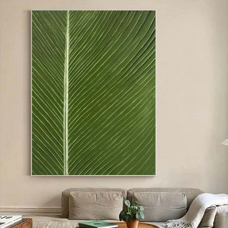 a large, vibrant green leaf as the central focus, hanging on a wall above a couch in a living room setting.