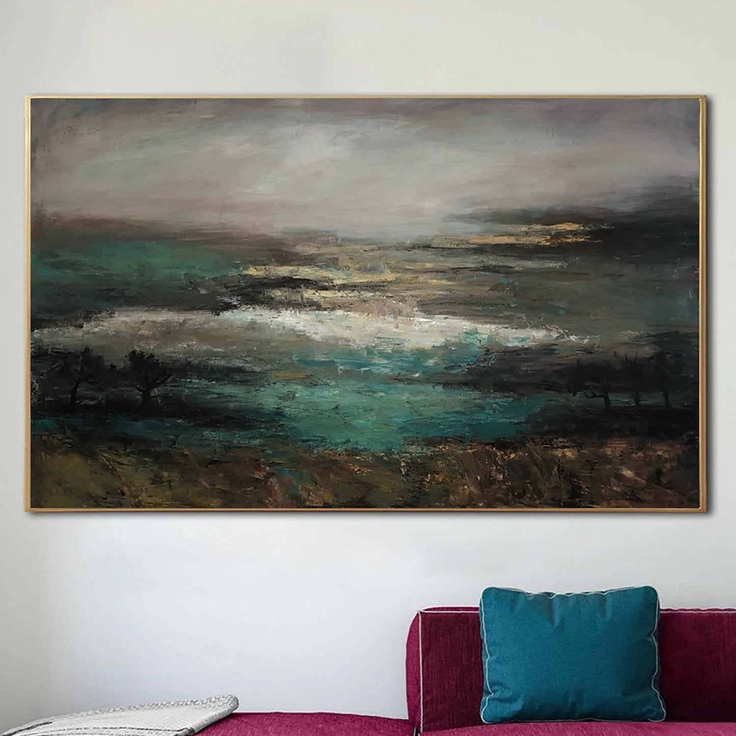a large landscape painting hanging on a wall above a red couch with a blue pillow.