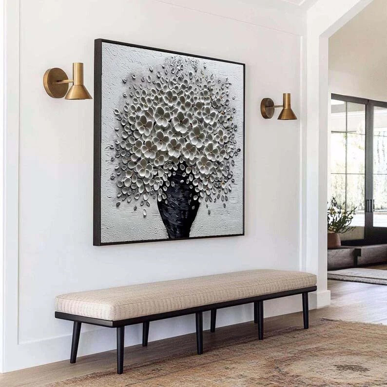 a modern interior design with a large black and white abstract painting of a tree on the wall, flanked by two wall sconces. In the foreground, there is a beige bench with a woven seat, and a rug on the floor.
