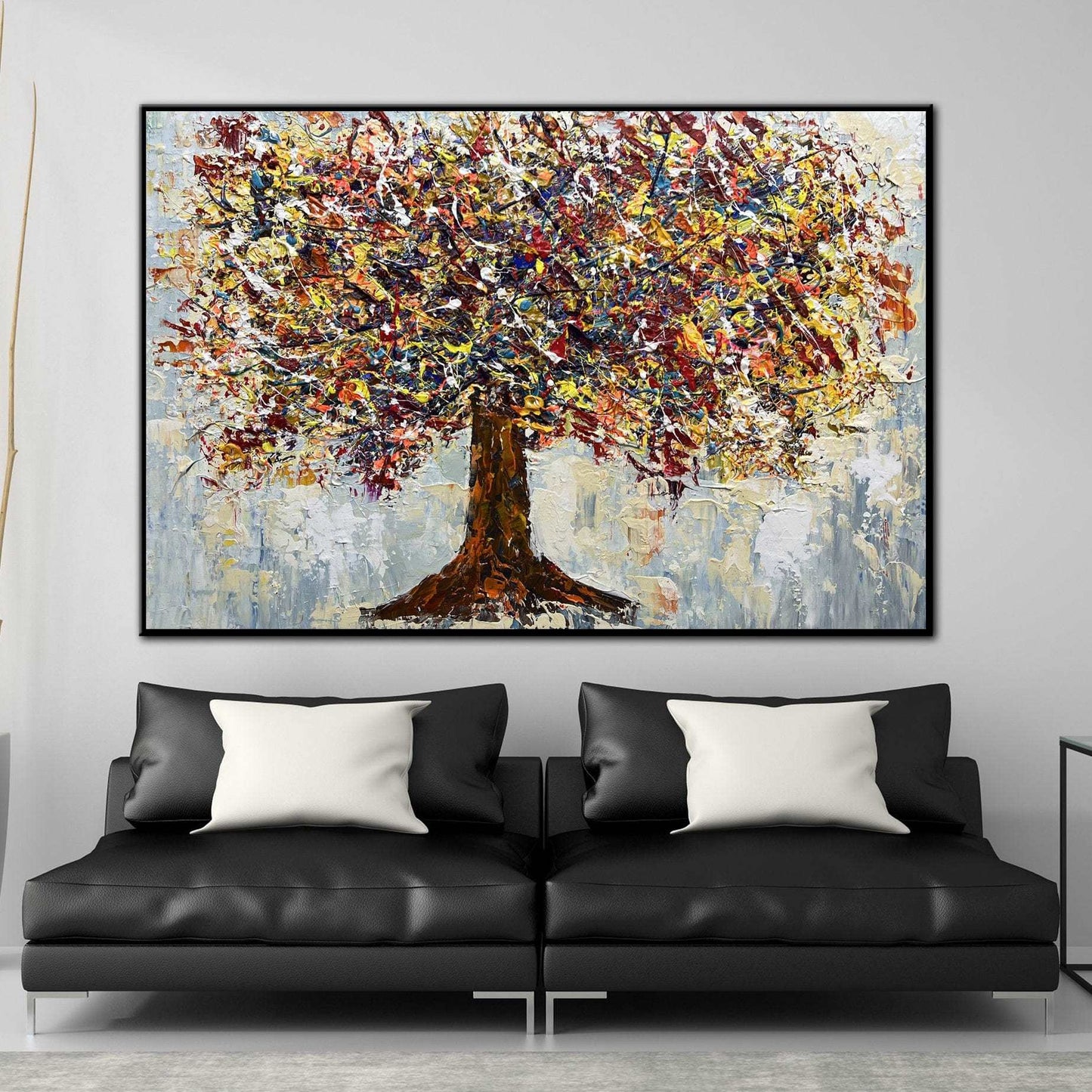 a large, colorful painting of a tree hanging on a wall above a black leather sofa with two white throw pillows.