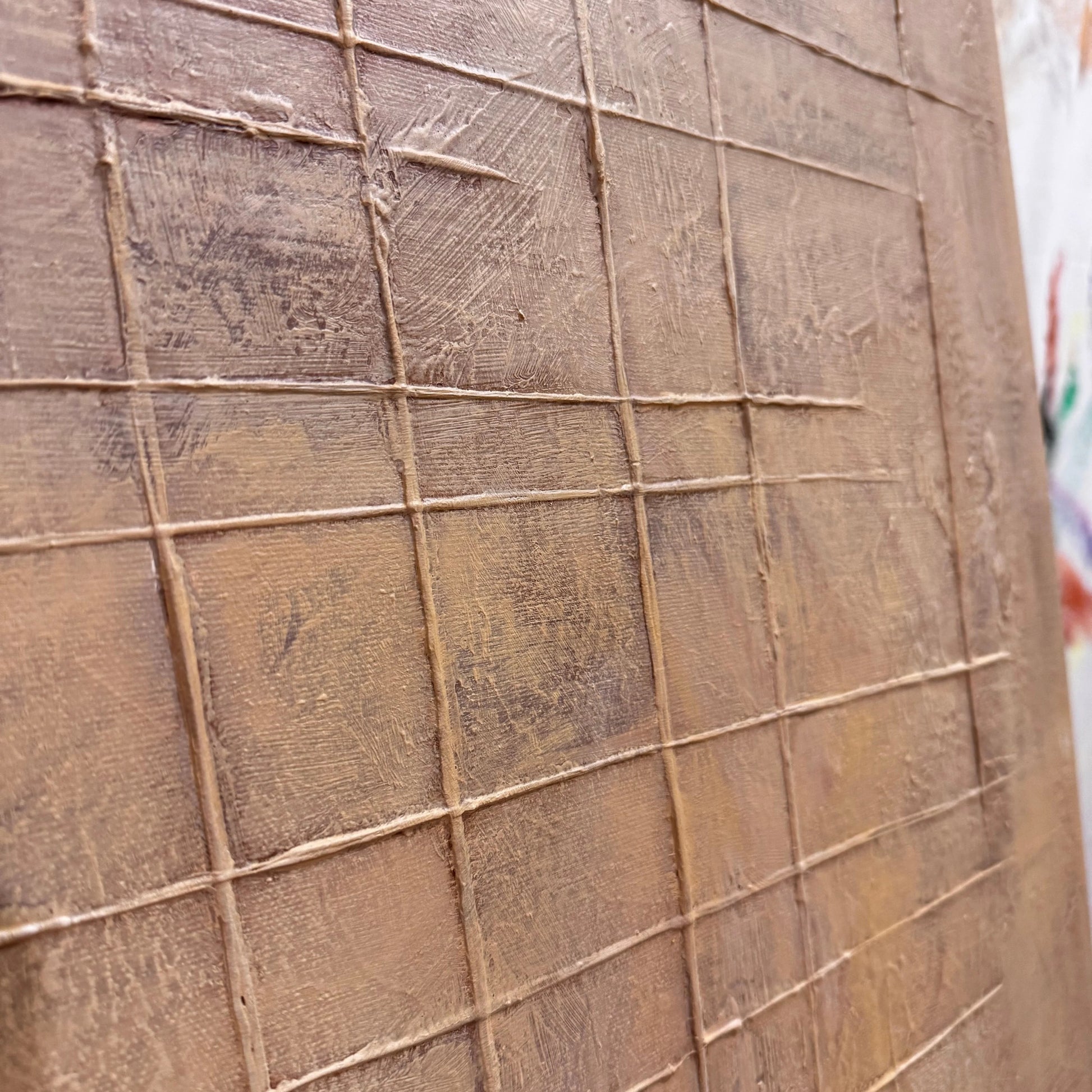 a close-up view of a textured surface, possibly a wooden panel or a canvas, with a grid-like pattern created by the lines and texture.