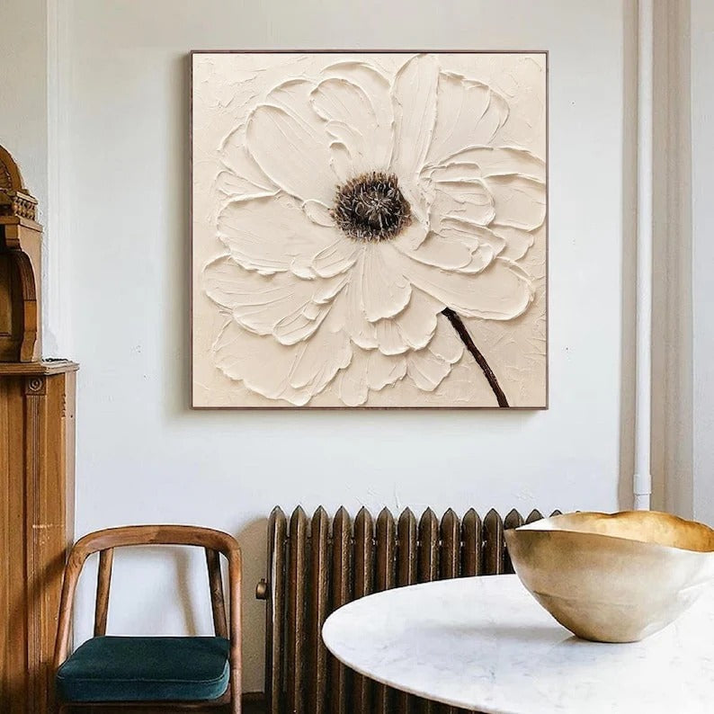 a large, white, floral-patterned painting hanging on a white wall above a wooden table with a bowl on it.