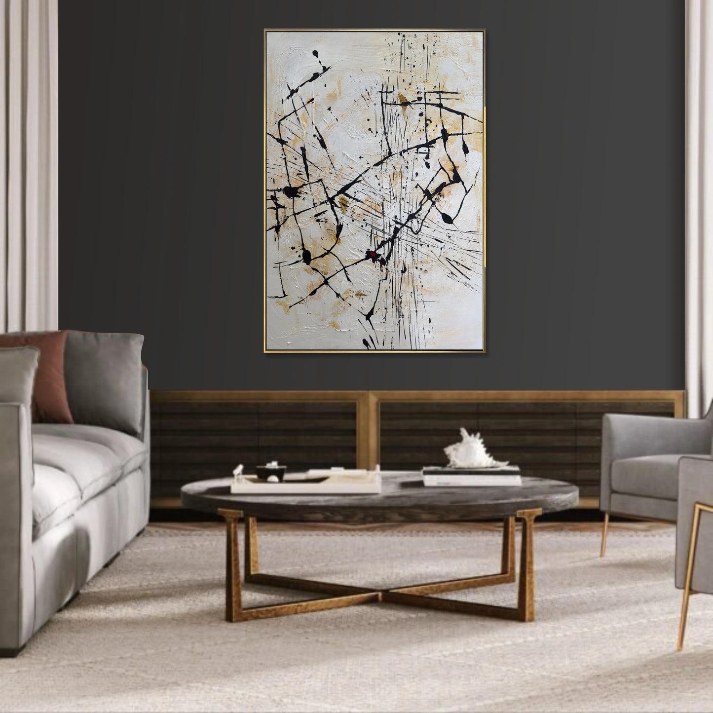 a modern living room with a large abstract painting hanging on the wall above a wooden coffee table. The room is furnished with a gray sofa, a gray armchair, and a gray ottoman. The coffee table has a white vase and a stack of books on it.
