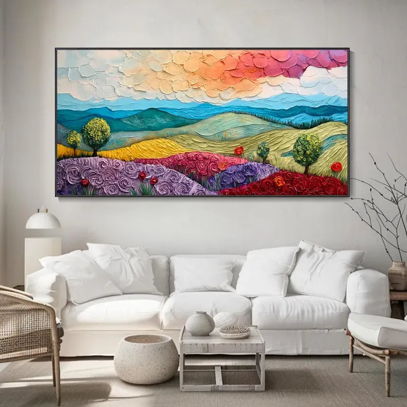 A large, colorful painting depicting a vibrant landscape with rolling hills, trees, and flowers adorns the wall above a white sofa in a cozy living room setting.