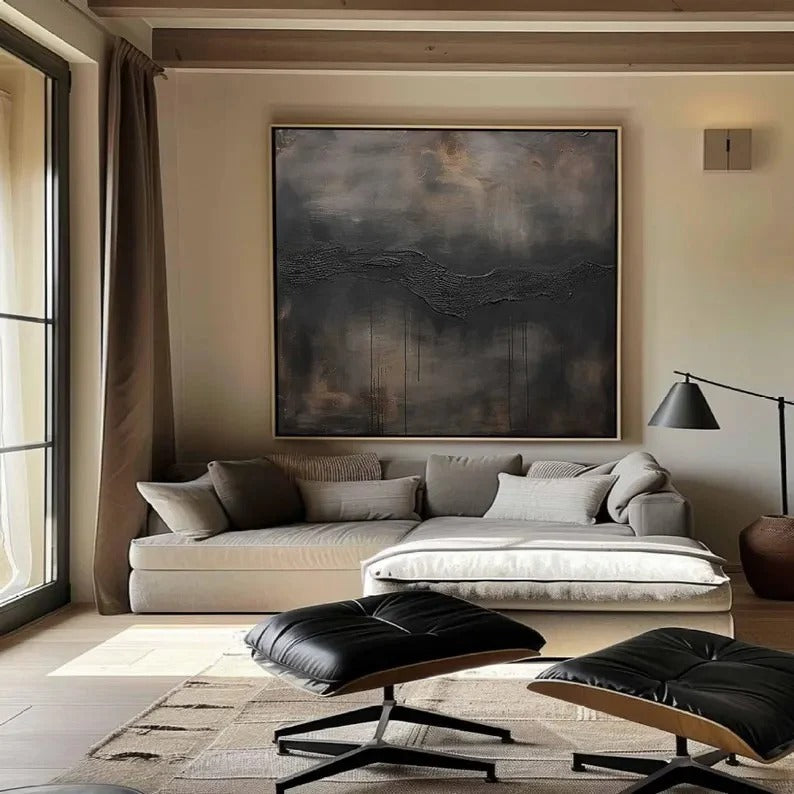 a modern living room with a large abstract painting on the wall, a gray sofa, a black leather ottoman, and a large window with curtains.