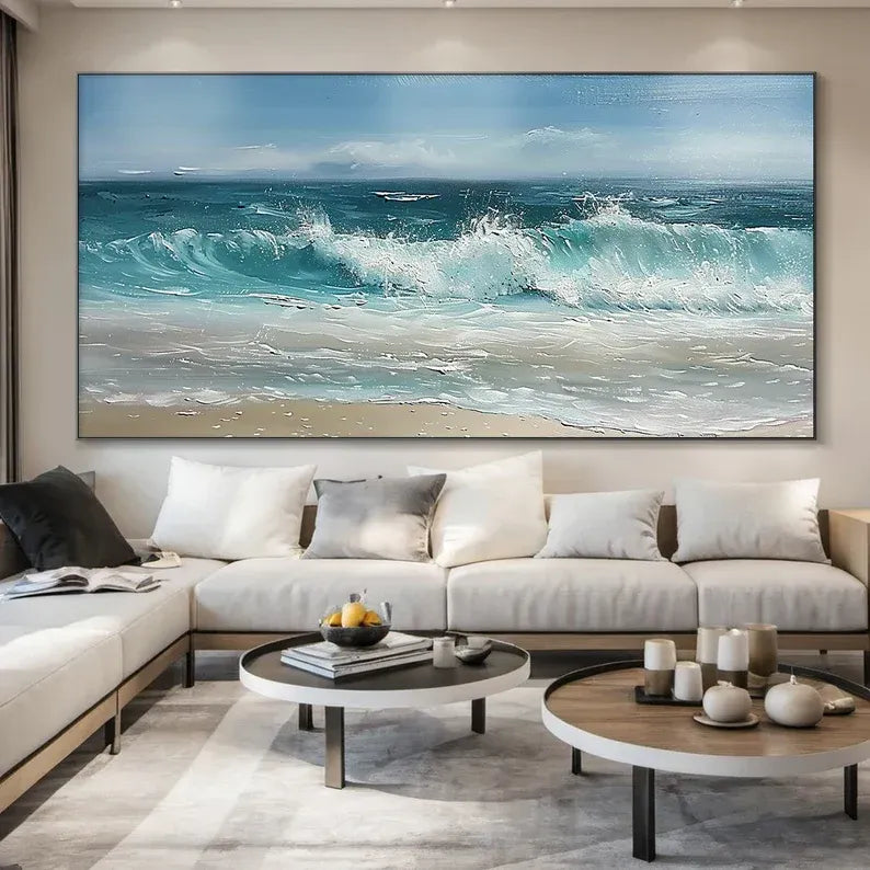 a large, vibrant painting of a serene ocean scene with crashing waves, set against a light blue sky with fluffy white clouds. The painting is hung on a wall above a comfortable-looking couch and a coffee table with various decorative items.