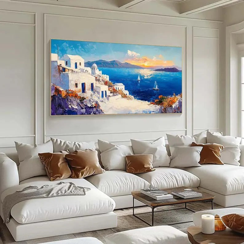 a large, colorful painting of a coastal town with white buildings, blue sky, and boats on the water, hanging on a wall above a white sofa with throw pillows.