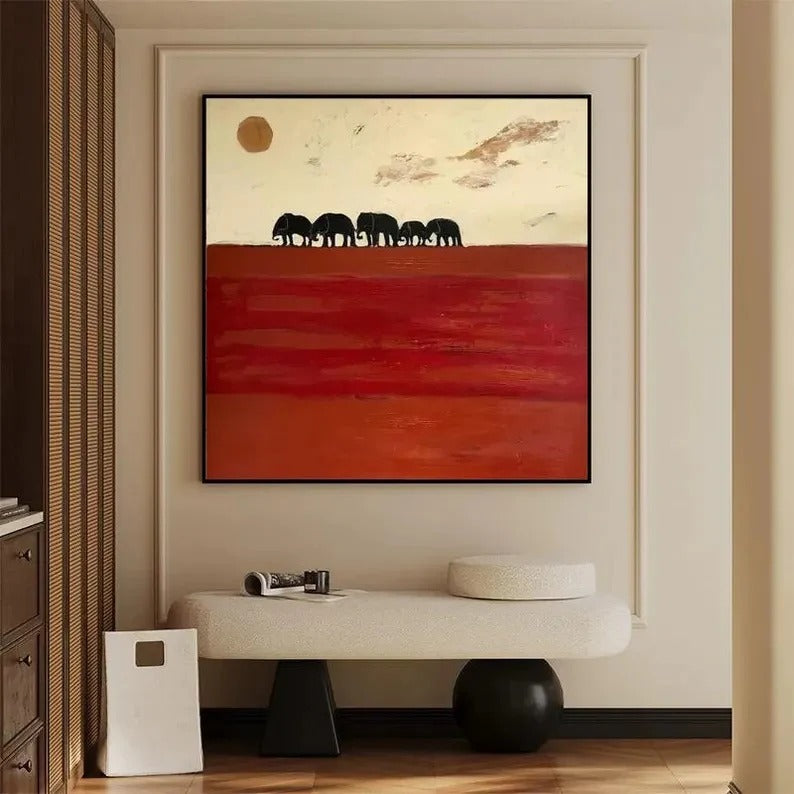 a large painting of elephants on a red background, hanging on a wall in a room with a bench and a small table.