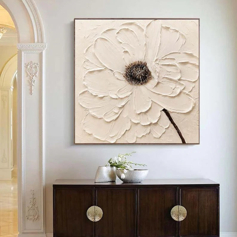 a large, square painting of a white flower hanging on a wall above a dark wooden cabinet.