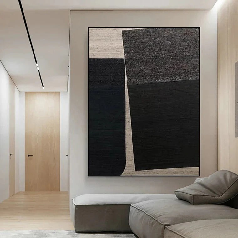 a modern living room with a large abstract painting hanging on the wall. The painting has a black and white color scheme, with a prominent diagonal line running through it. The room has a minimalist design, with a gray sofa and a wooden floor.