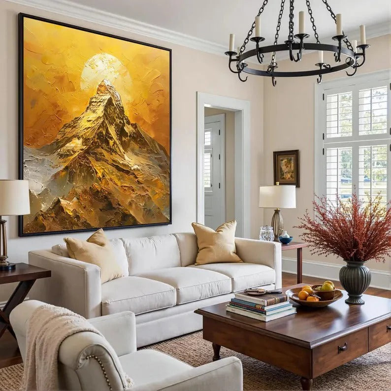 a cozy living room with a large, vibrant painting of a mountain landscape hanging on the wall. The room is furnished with a white sofa, a wooden coffee table, and a chandelier overhead. The overall decor has a warm and inviting atmosphere.