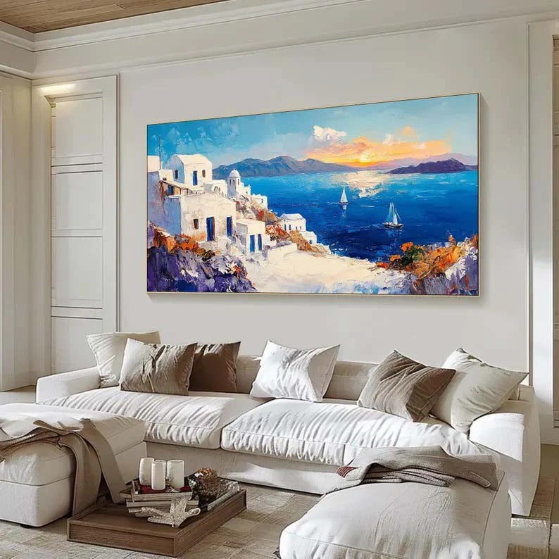 a large, colorful painting of a coastal town with white buildings, blue sky, and boats on the water. The painting is displayed on a wall above a white sofa in a living room setting.