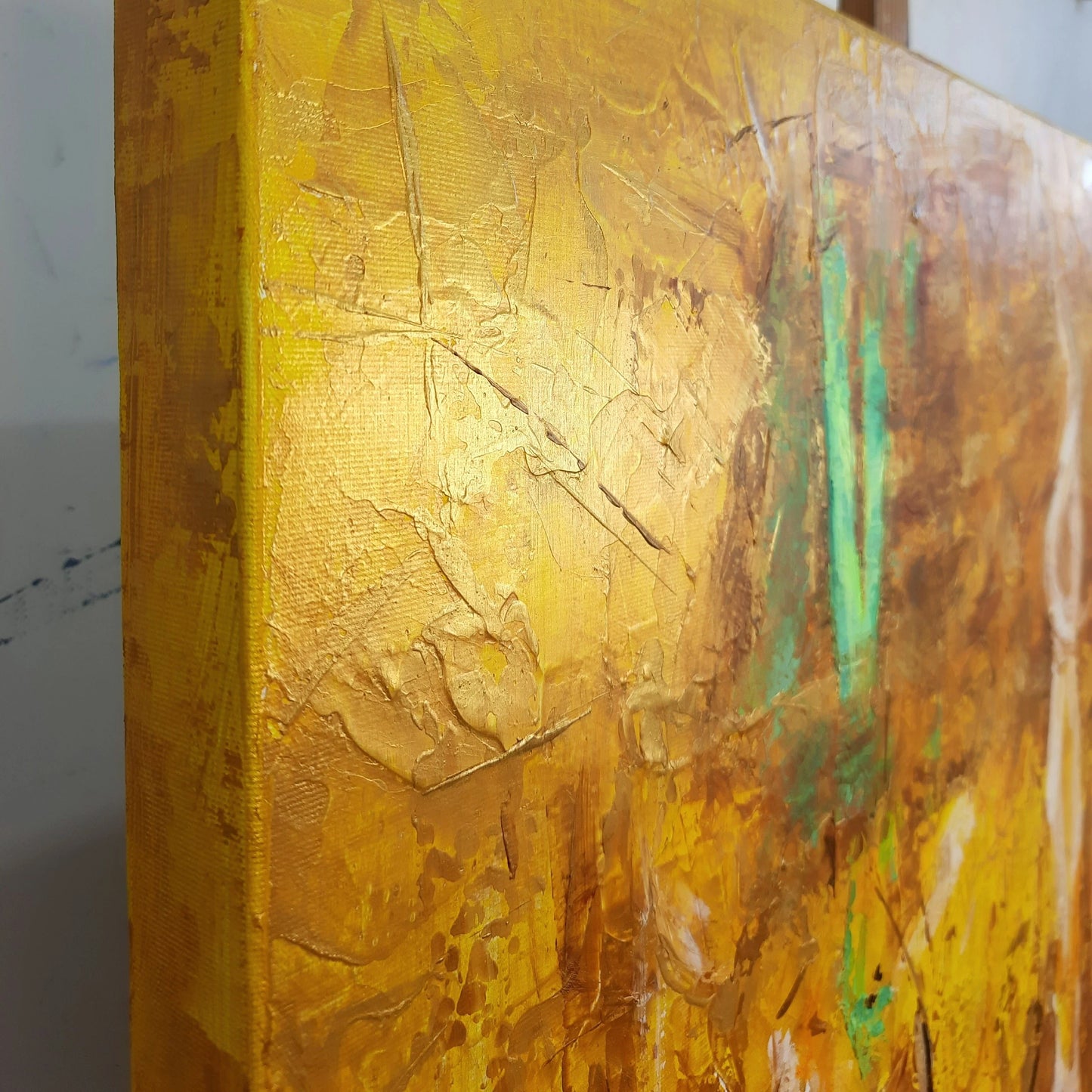 The image is a close-up of a textured yellow surface, possibly a painting or canvas, with a green and brown color palette.