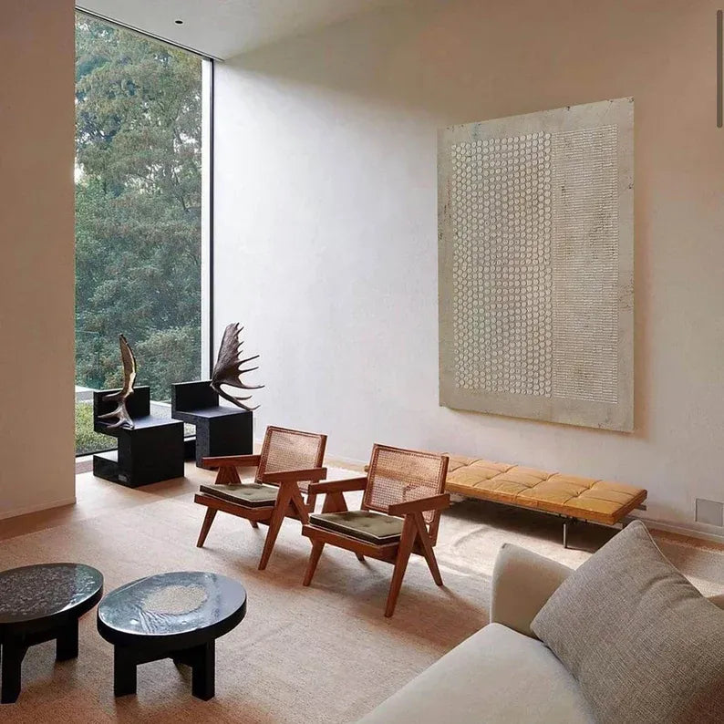 a modern living room with a large window overlooking a wooded area. The room features a white color scheme, with a wooden bench, two wooden chairs, and a large abstract artwork on the wall.