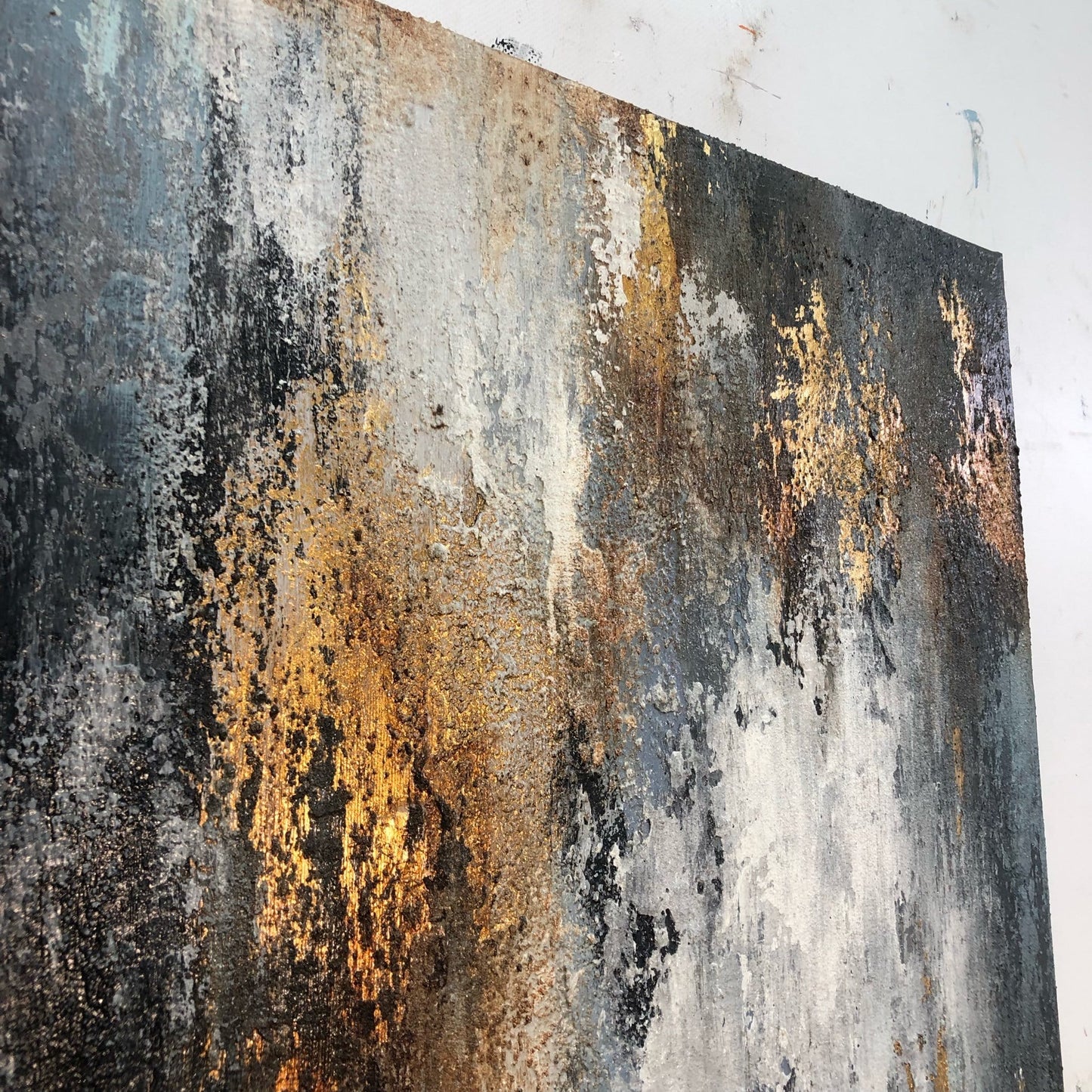 The image is a close-up of a textured, abstract painting with a mix of black, white, and gold colors. The painting appears to be a large canvas or artwork, with a rough, textured surface that gives it a weathered, aged appearance.