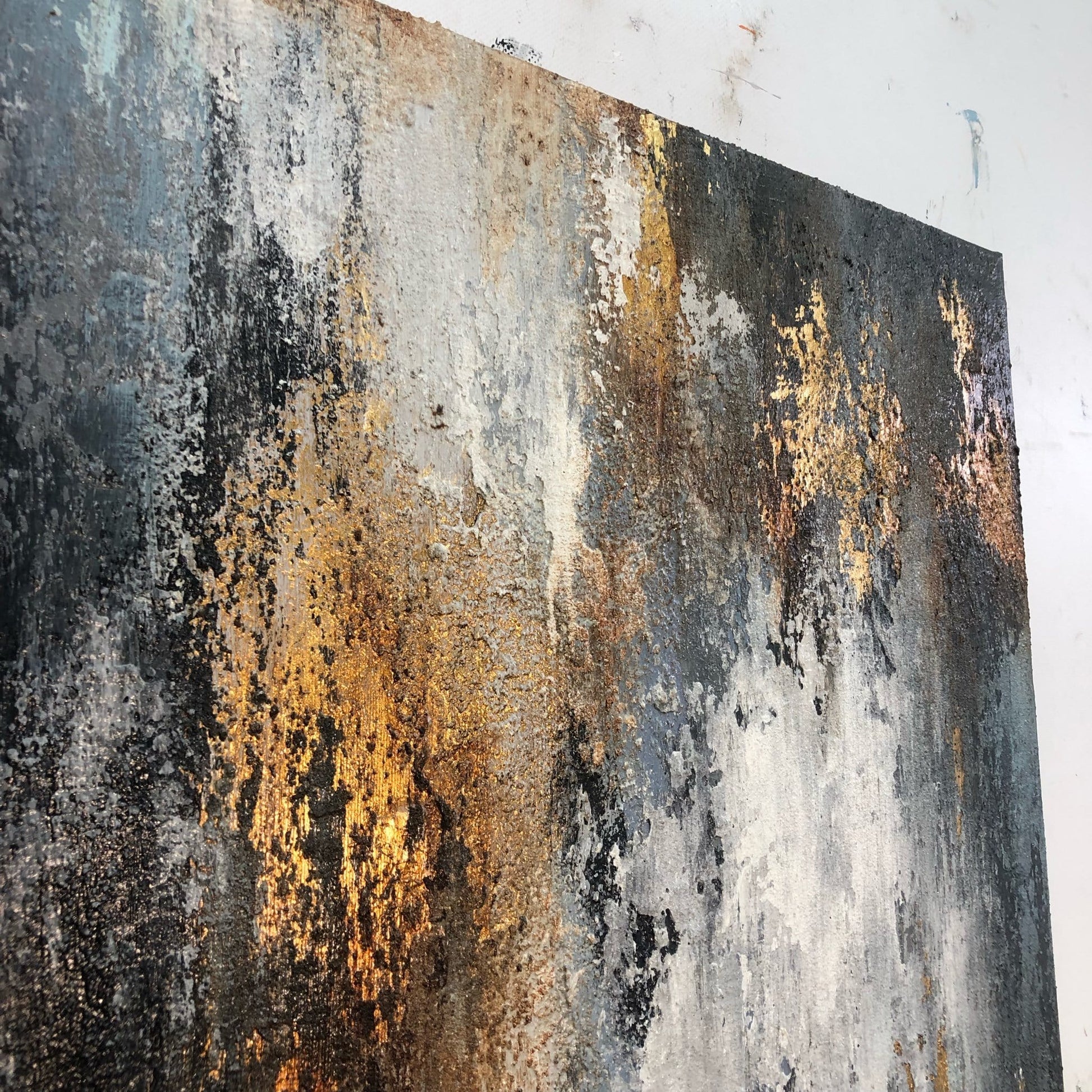 The image is a close-up of a textured, abstract painting with a mix of black, white, and gold colors. The painting appears to be a large canvas or artwork, with a rough, textured surface that gives it a weathered, aged appearance.