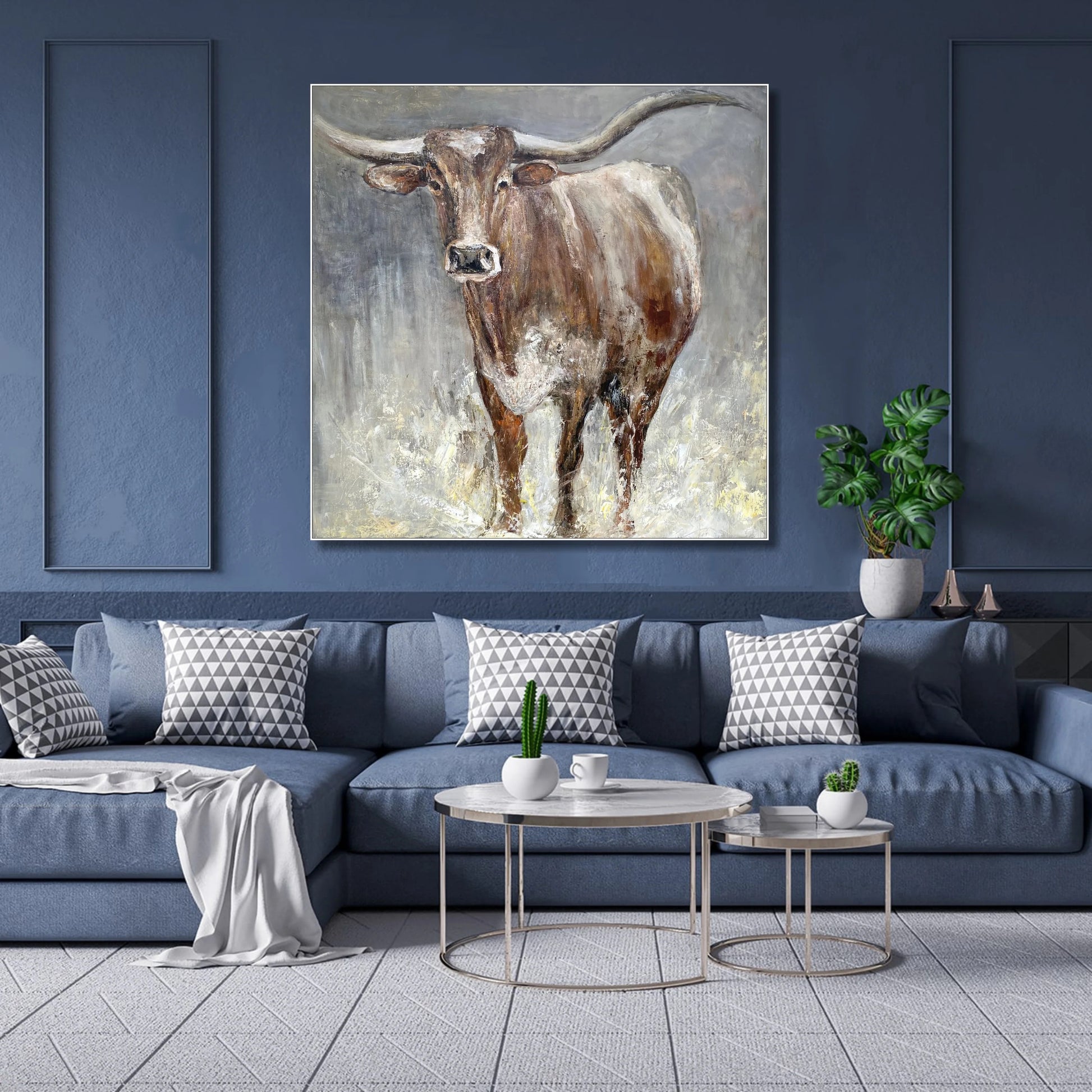 a large painting of a bull with horns hanging on a blue wall above a blue couch with patterned pillows.
