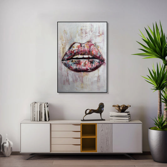 a modern art piece with a large, colorful painting of lips hanging on a white wall above a white cabinet with drawers. The cabinet also has a small sculpture of a horse on top of it. The room has a potted plant and some books, creating a stylish and contemporary atmosphere.