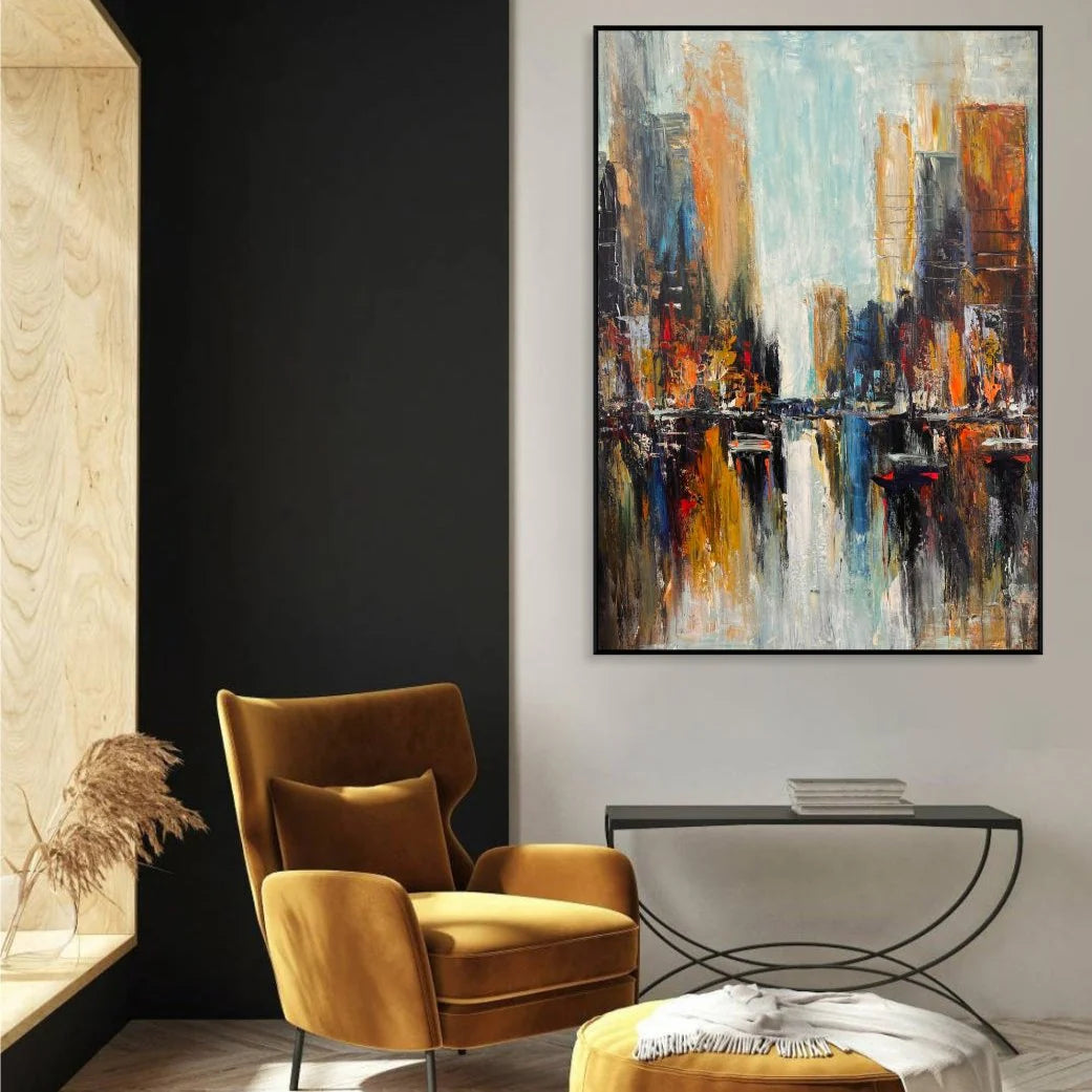 a modern living room with a large abstract painting of a cityscape hanging on the wall. The painting is predominantly blue, orange, and yellow, creating a vibrant and dynamic visual effect. The room is furnished with a yellow armchair and a black side table, providing a cozy and stylish seating area. The overall design and color scheme of the room create a visually appealing and contemporary atmosphere.