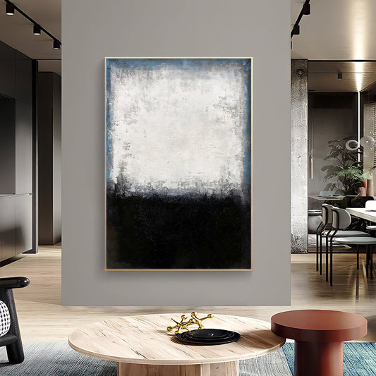 a modern living room with a large abstract painting hanging on the wall. The painting has a black and white color scheme, with a predominantly white background and a black bottom half. The room is furnished with a wooden coffee table, a red stool, and a black and gold decorative piece. The overall design and color scheme create a contemporary and stylish atmosphere in the living space.