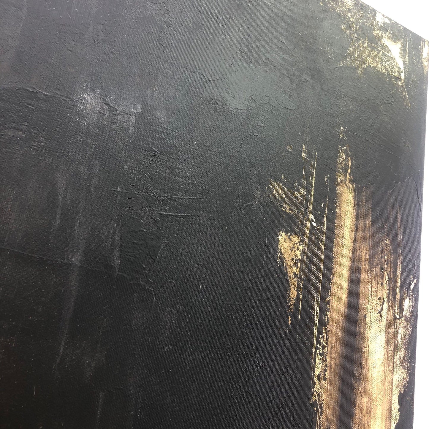 The image is a close-up of a textured black surface with a gold-colored splatter or stroke on it.