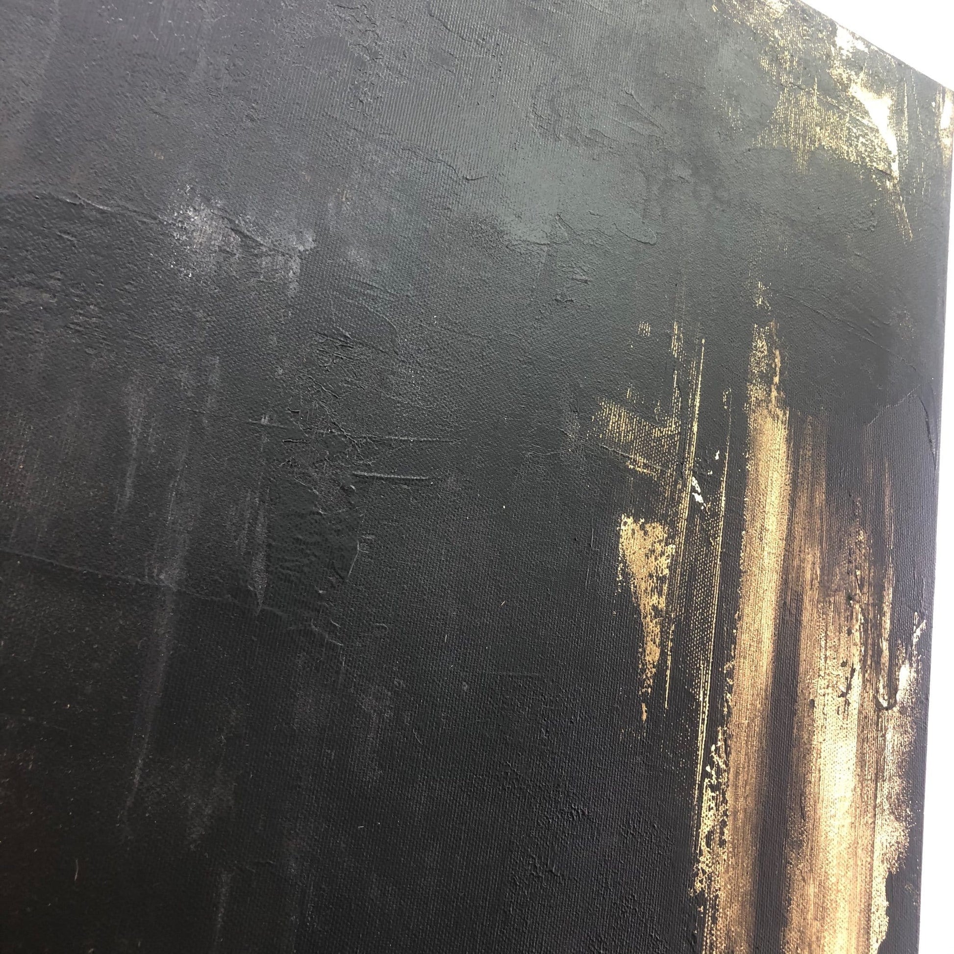 The image is a close-up of a textured black surface with a gold-colored splatter or stroke on it.