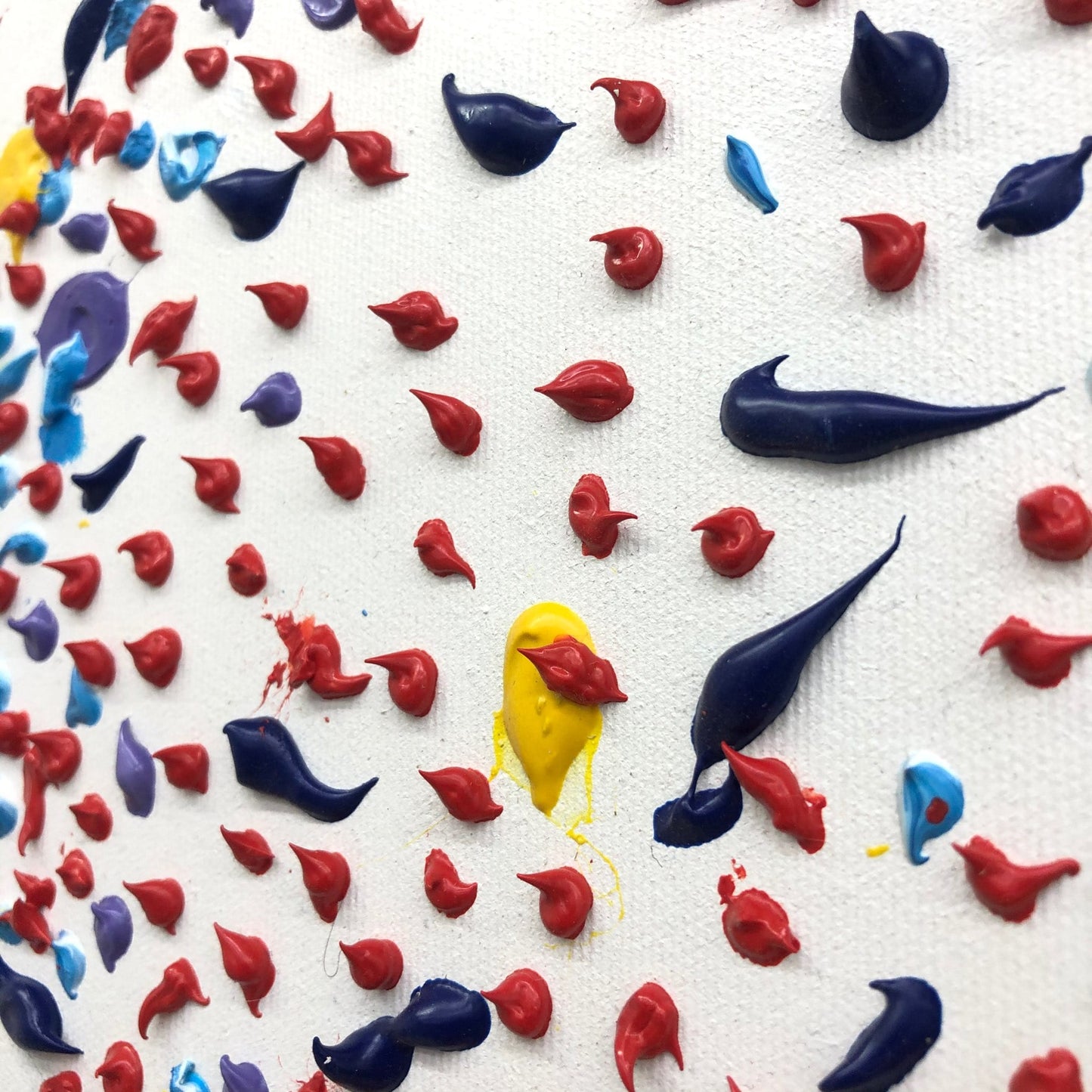 The image is a close-up of a white surface with a variety of colorful paint splatters and drips, including red, blue, yellow, and purple paint.