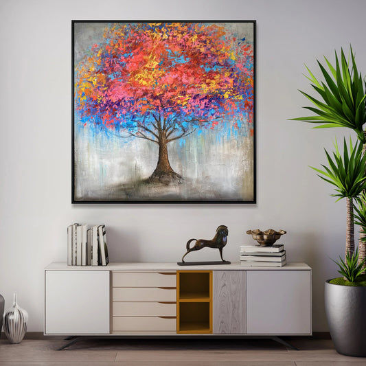 a large painting of a colorful tree hanging on a wall above a white cabinet with drawers. The cabinet has a decorative horse figurine on top of it. The painting is surrounded by several books, and there is a potted plant in the background.