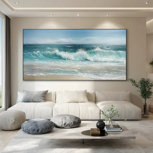 a modern living room with a large, vibrant painting of a beach scene hanging on the wall. The painting features a blue sky, crashing waves, and a sandy beach, creating a serene and relaxing atmosphere. The room is furnished with a white sofa and a coffee table, and there are some decorative elements such as a potted plant and a vase.