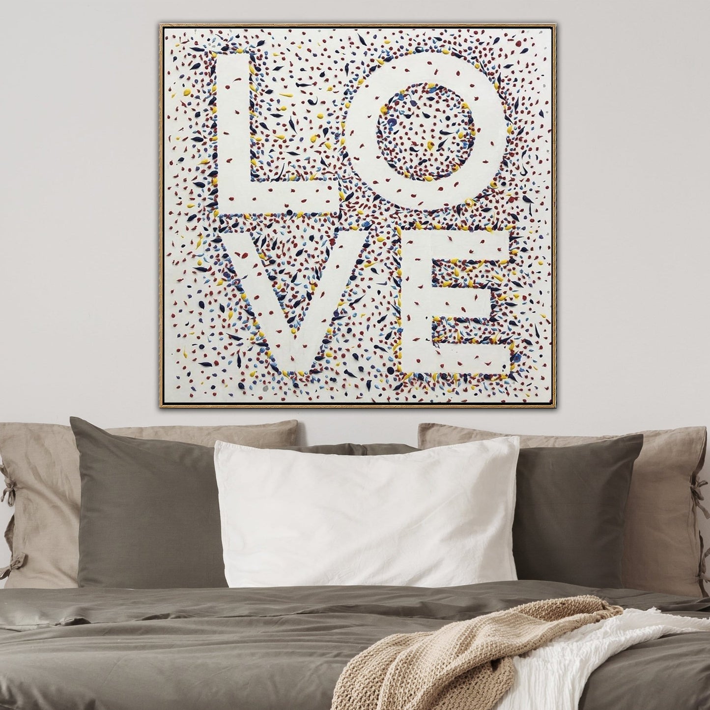a large, colorful painting of the word "LOVE" in the shape of a heart on a wall above a bed with pillows.
