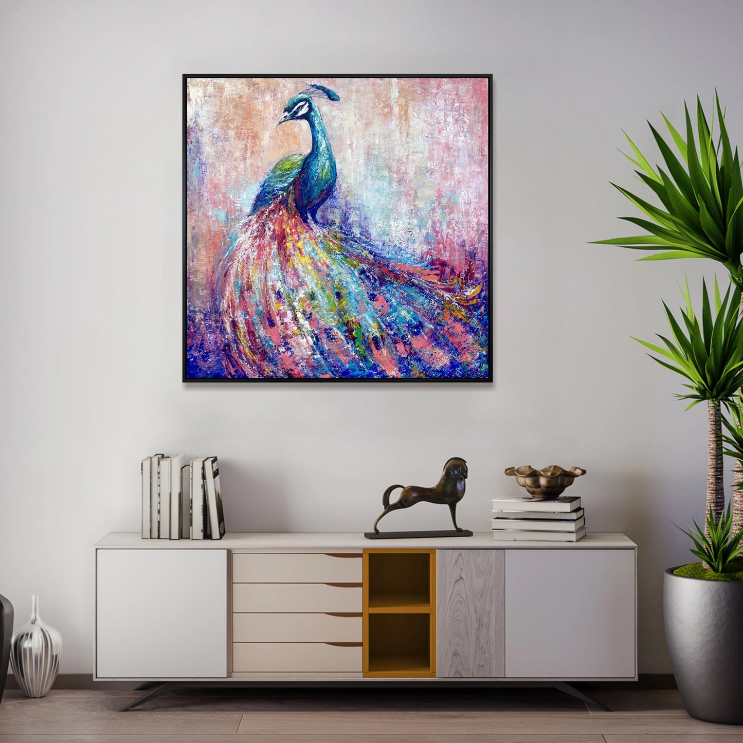 a large, colorful painting of a peacock displayed on a wall above a white cabinet with drawers. The cabinet also has a small statue of a horse and a stack of books on top.