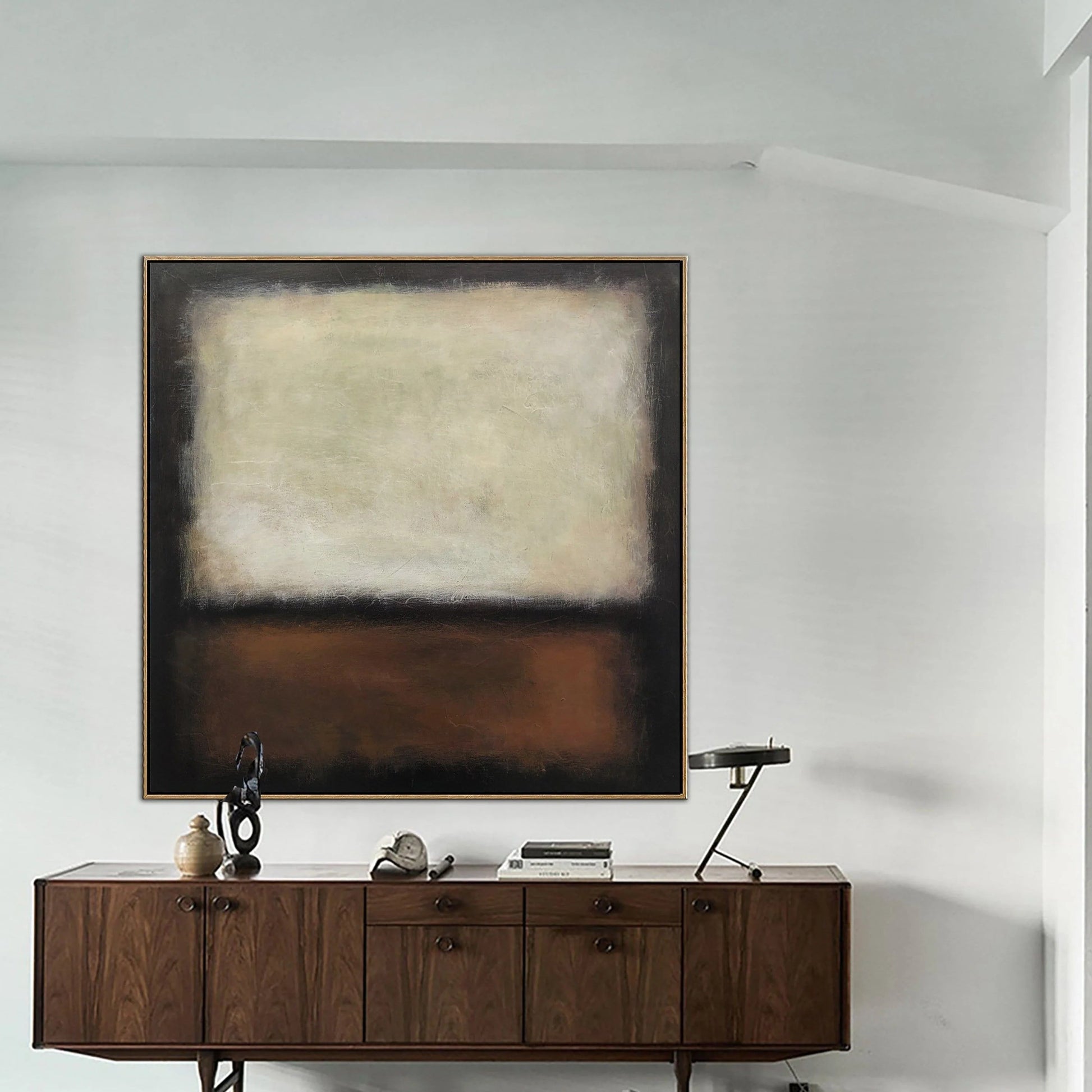 a large abstract painting hanging on a white wall above a wooden cabinet with drawers. The cabinet has a small sculpture and a lamp on top of it.