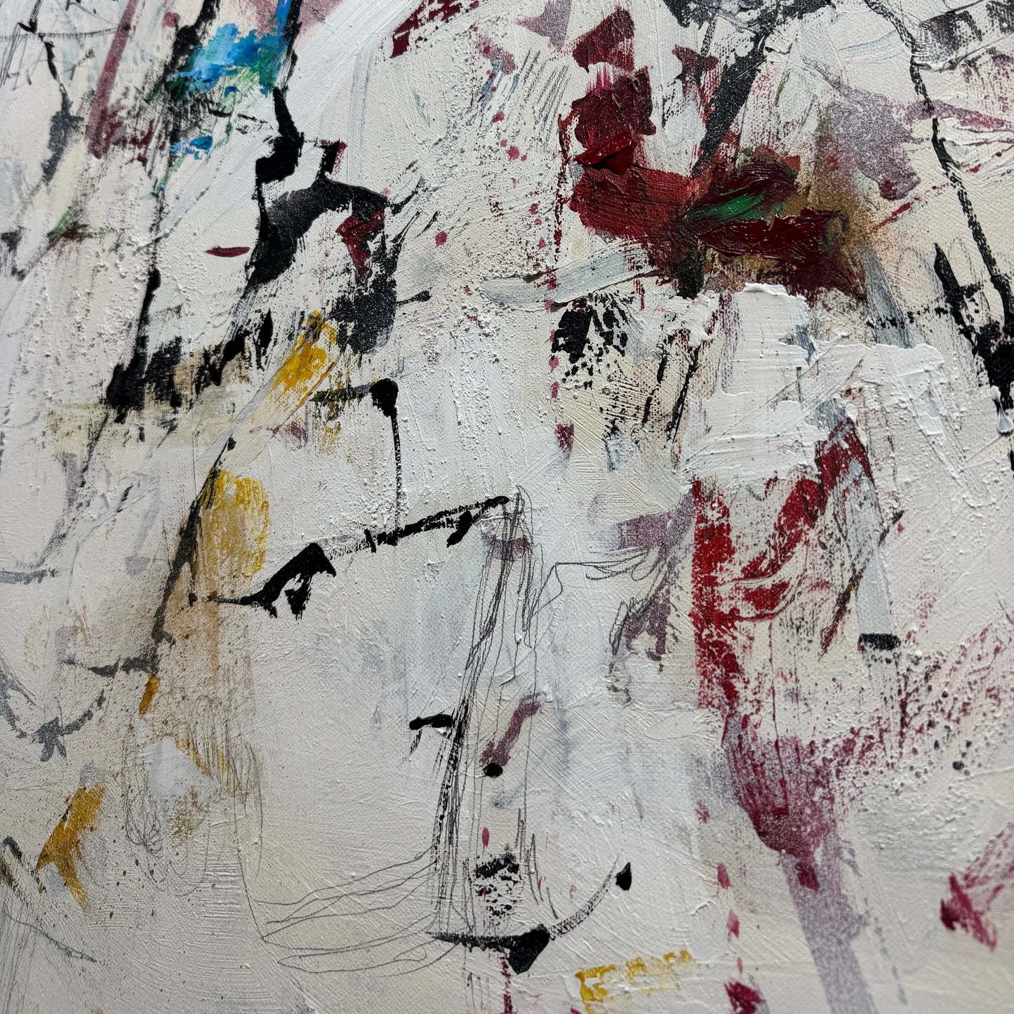 The image is a close-up of a white surface with a variety of abstract and expressive brushstrokes in different colors, including red, black, yellow, and blue. The brushstrokes appear to be spontaneous and expressive, creating a dynamic and visually interesting composition.