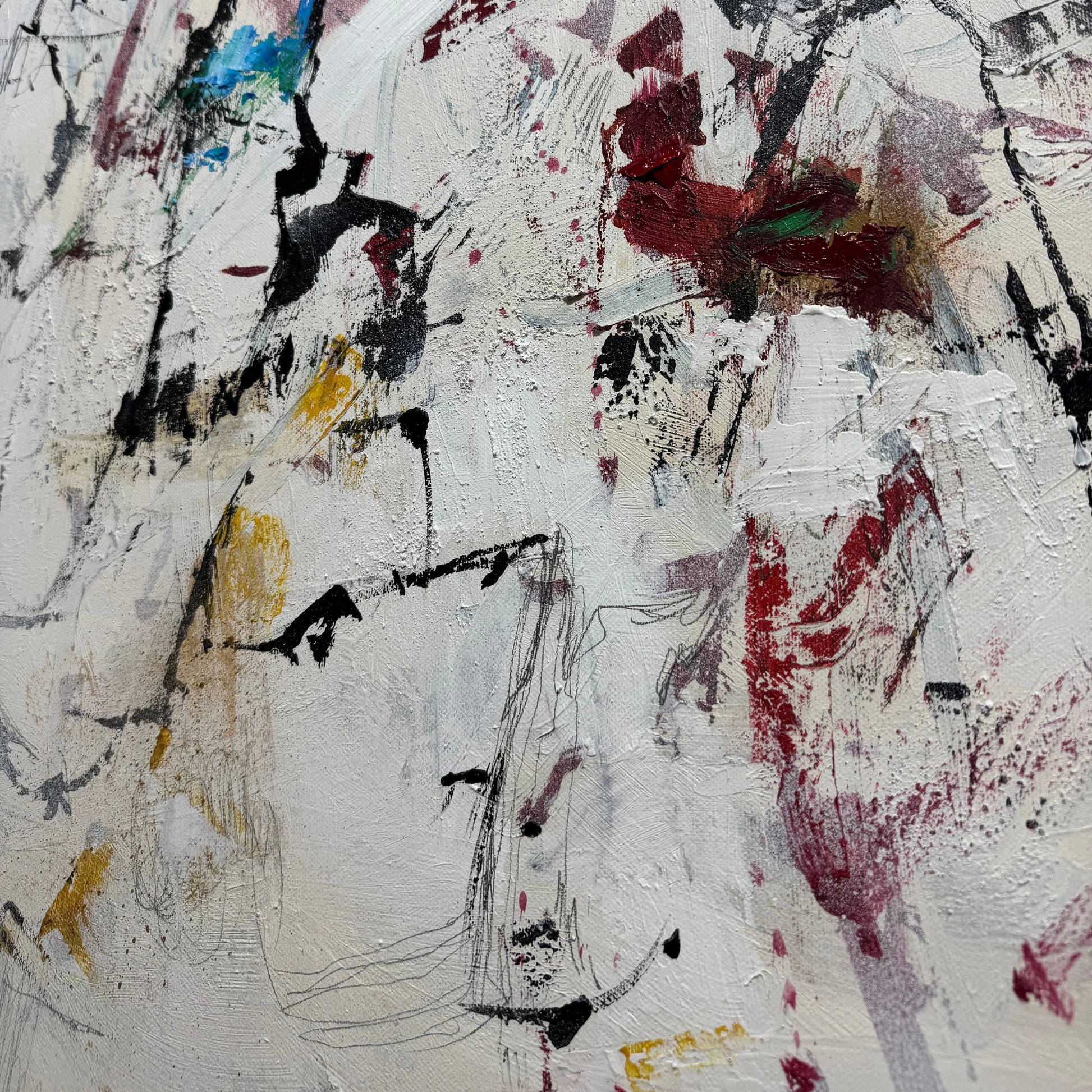 The image is a close-up of a white surface with a variety of abstract and expressive brushstrokes in different colors, including red, black, yellow, and blue. The brushstrokes appear to be spontaneous and expressive, creating a dynamic and visually interesting composition.
