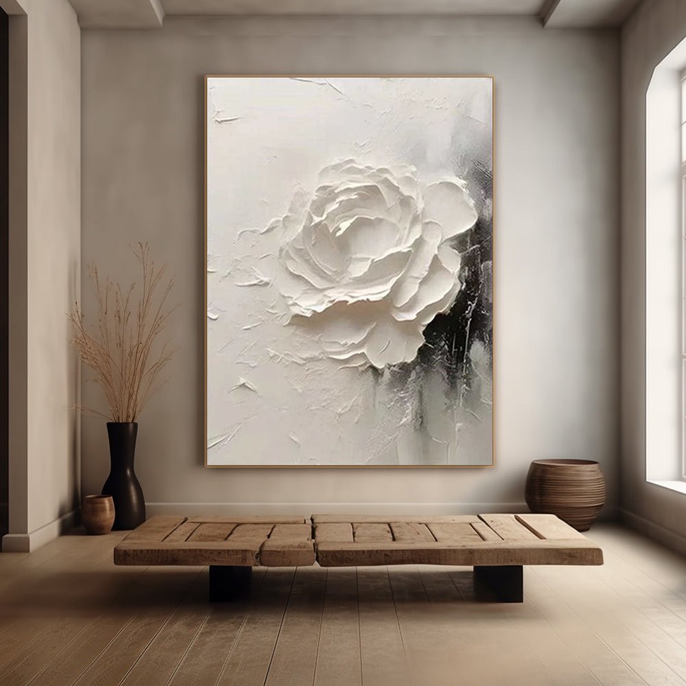 a large white flower painting hanging on a wall, with a wooden bench in front of it. There are also two vases on the floor, one on the left and one on the right.