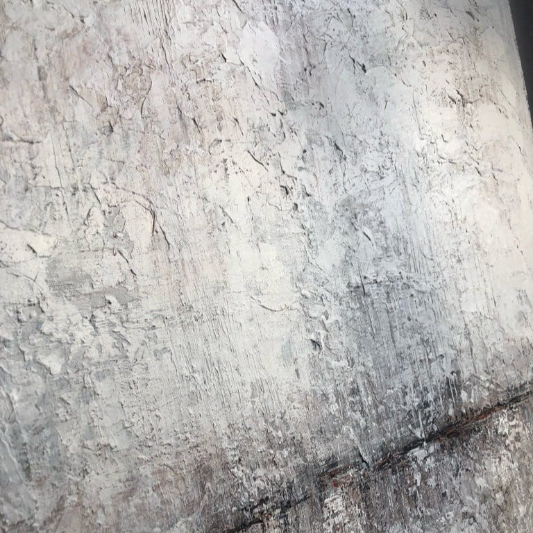 a close-up view of a textured, weathered surface, possibly a wall or a piece of art. The surface appears to be made of a material that has a rough, uneven texture, with visible cracks and crevices. The overall color palette of the image is muted, with shades of gray and white dominating the scene.