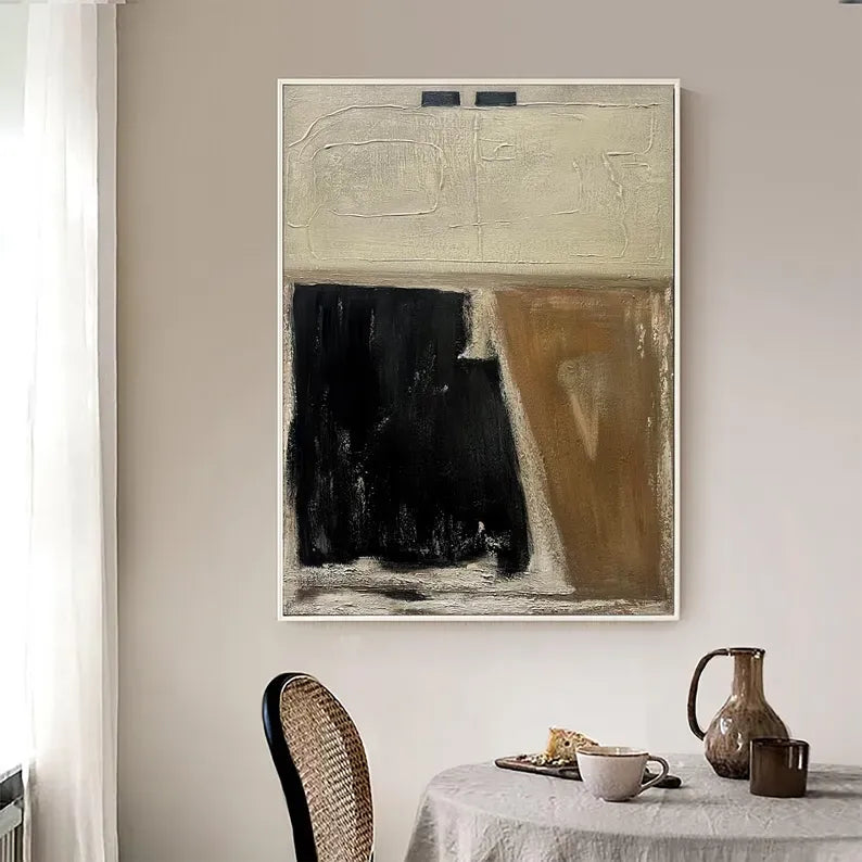 a large abstract painting hanging on a wall above a dining table with a white tablecloth. The painting has a black and white color scheme, with a prominent brown section. The dining table is set with a white vase, a brown pitcher, and a white coffee cup.