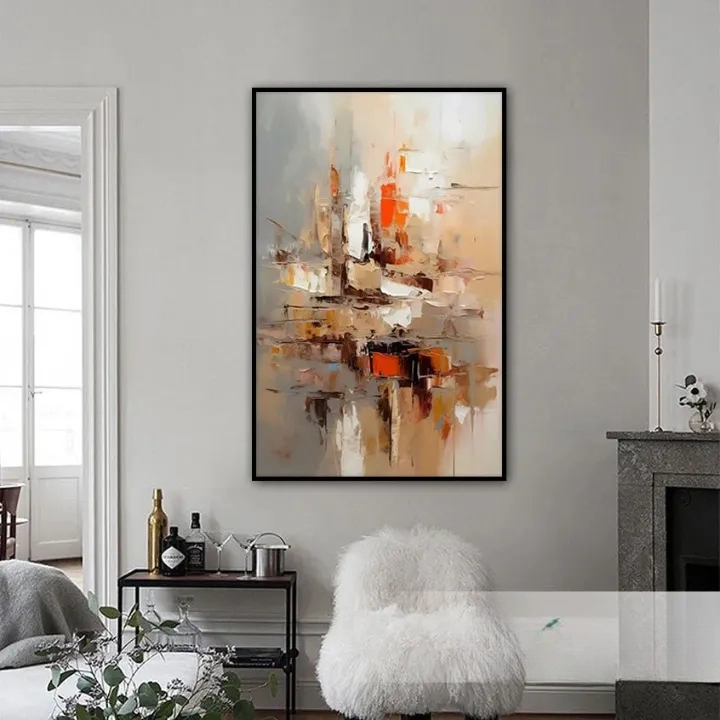 a large abstract painting hanging on a wall in a living room. The painting has a warm color palette with shades of orange, brown, and beige. The room has a cozy and inviting atmosphere, with a fireplace, a white chair, and a small table with various items on it.
