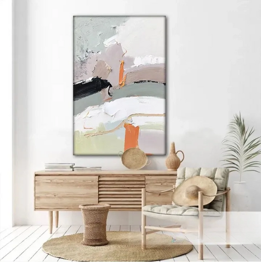 a modern living room with a large abstract painting hanging on the wall above a wooden dresser. The dresser has a wicker basket and a vase on it. There is a chair with a hat on it, and a plant is visible in the background.