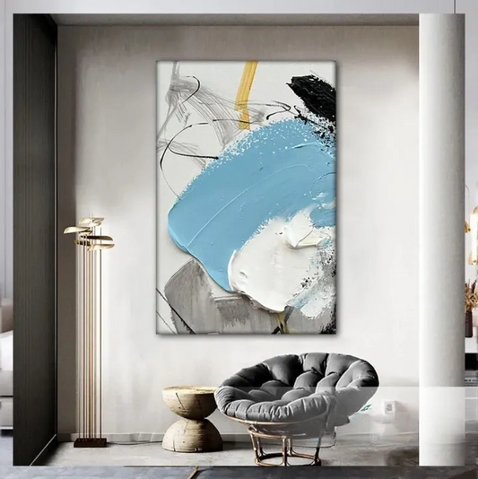 a modern living room with a large abstract painting hanging on the wall. The painting has a mix of blue, white, and black colors, creating a striking contrast. In the foreground, there is a gray armchair and a wooden side table, adding to the contemporary aesthetic of the room.