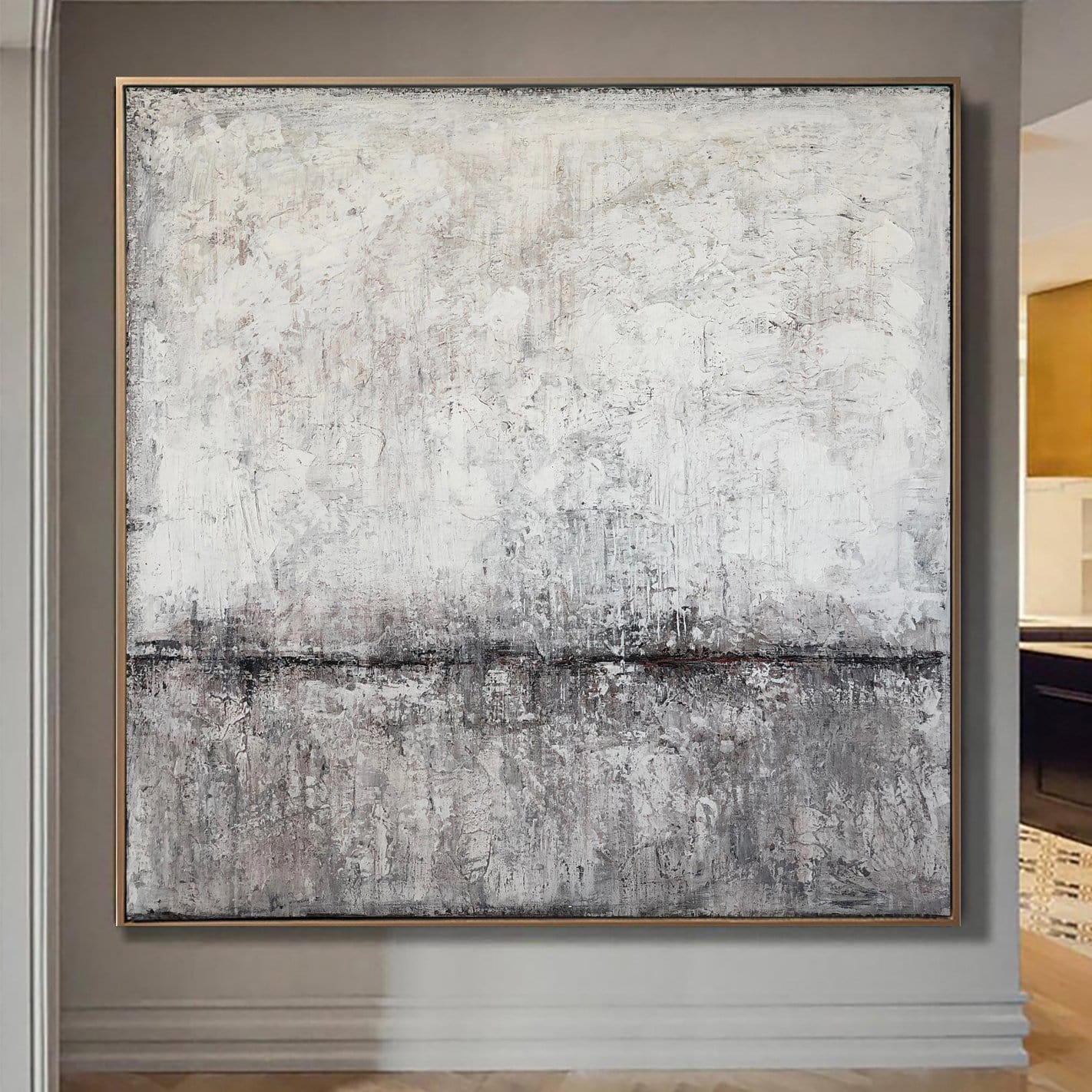 a large, abstract painting hanging on a wall. The painting has a predominantly white and gray color scheme, with some areas of black and brown adding contrast. The painting is framed in a gold frame, which complements the overall color palette. The painting appears to be a modern art piece, showcasing the artist's skill and creativity.