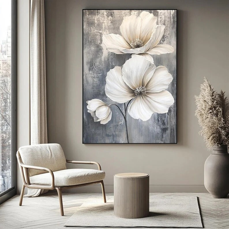 a large painting of white flowers hanging on a wall, with a beige armchair and a small round table in the foreground.