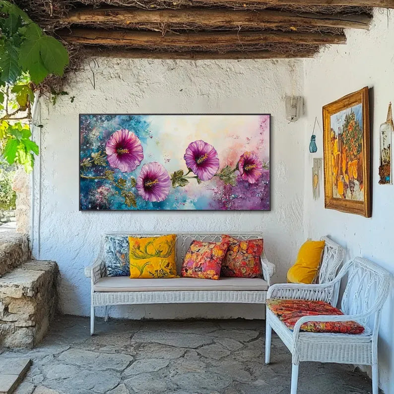 a cozy outdoor seating area with a large painting of pink flowers hanging on the wall above a white wicker bench. The bench is adorned with colorful pillows, and there are two additional chairs in the space. The overall atmosphere of the scene is warm and inviting, with the vibrant colors of the flowers and the comfortable seating arrangement creating a pleasant and relaxing environment.