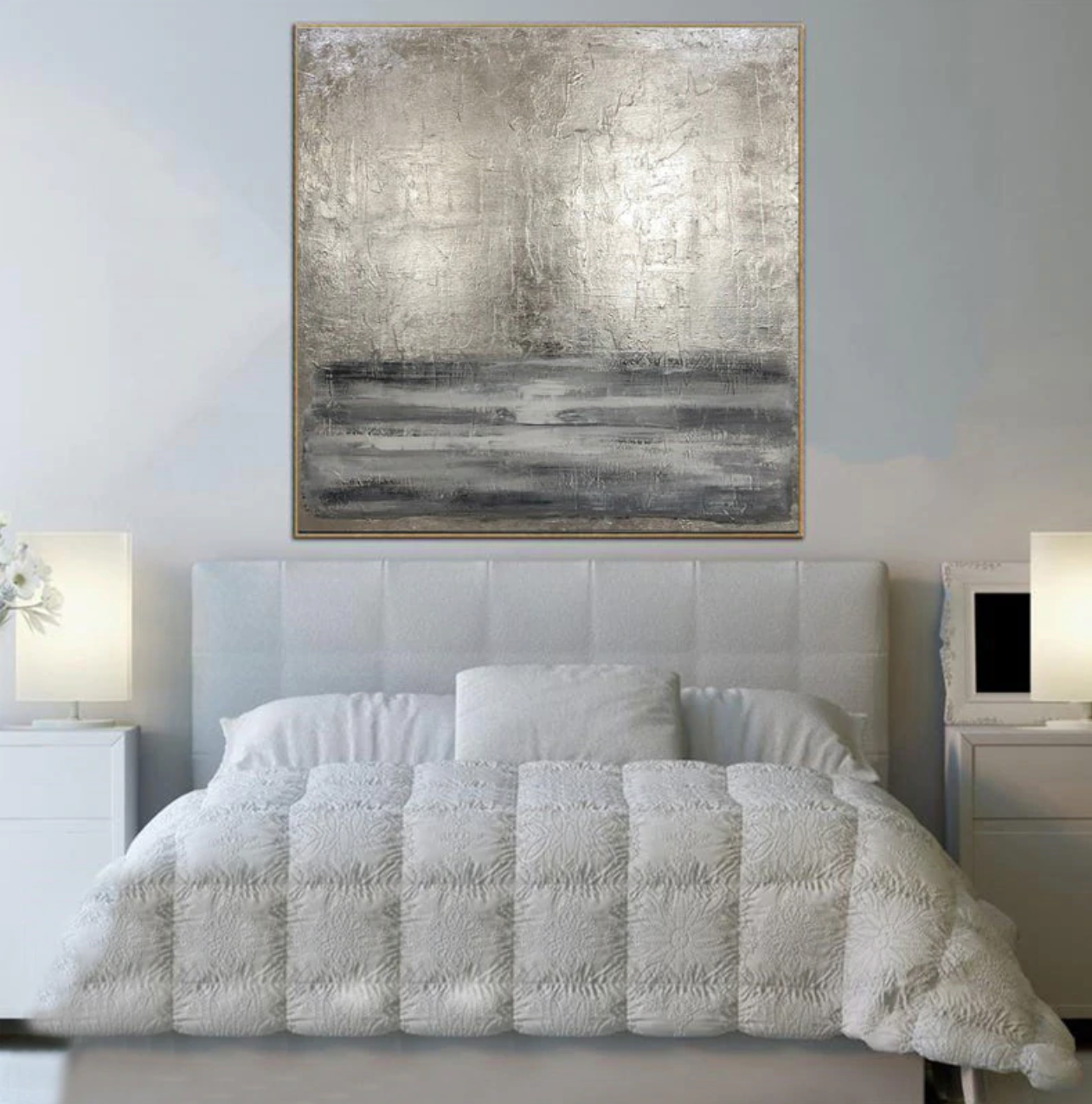 a white bed sitting under a painting on a wall